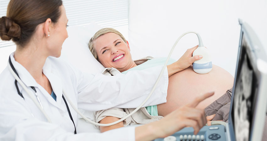 Happy female doctor showing woman her baby on ultrasound at the hospital