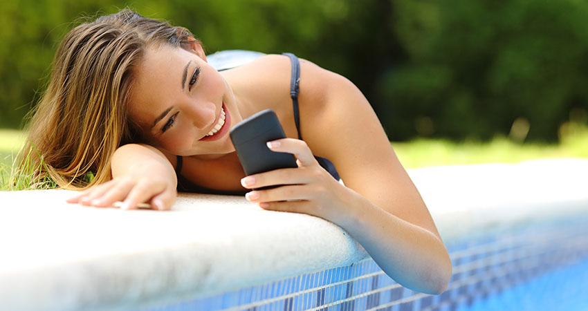 Woman using a smart phone in a poolside in summer
